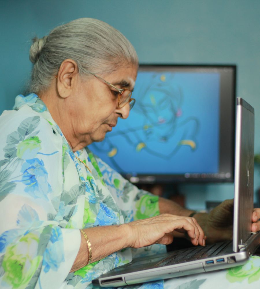 An elderly Indian woman in a saree confidently using a laptop